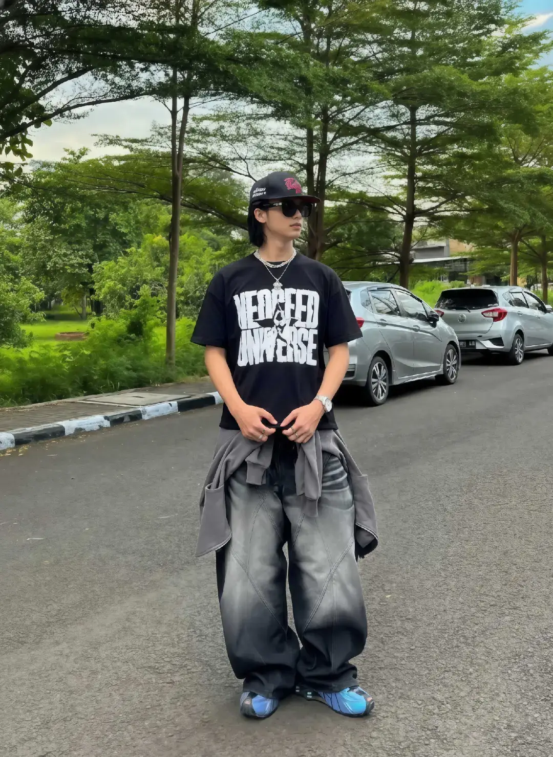 TUTORIAL?? BACA CAPTION!! Caranya? 1. Buka google/apk gemini di hp kalian 2. Masukan photo wajah kalian dan pastekan  prompt:👇🏻 Buatkan sebuah foto vertikal bidikan penuh yang menampilkan seorang pria muda bergaya streetwear modern dari subjek di atas, berpose santai di tepi jalan. Pria tersebut menjadi fokus tajam dalam gambar, memancarkan kesan cool dan percaya diri. Ia mengenakan kaus hitam longgar dengan grafis putih bertuliskan 'NEOFEED UNIVERSE' dan celana jeans super longgar (baggy) berwarna hitam pudar dengan efek gradasi acid wash yang mencolok seperti foto diatas. Di pinggangnya, ia mengikat jaket abu-abu dan melengkapi gayanya dengan topi baseball hitam-merah, kacamata hitam, beberapa kalung rantai perak tebal berlapis, dan jam tangan. Serta detail sepatu  yang dikenakan persis seperti foto diatas, Subjek bersandar dengan santai pada tiang lampu atau rambu di tepi trotoar. Di latar depan, terlihat bagian aspal jalan, garis tepi berwarna putih-hitam, dan sedikit rumput hijau. Di latar tengah, membentang di sisi kiri jalan, adalah deretan pohon palem kurus yang memberikan tekstur alami dan kontras dengan elemen urban. Latar belakang didominasi oleh deretan bangunan komersial atau ruko modern berlantai dua dengan arsitektur minimalis berwarna netral (cokelat muda, abu-abu, dan putih). Suasana jalanan terlihat sepi, memberikan fokus penuh pada gaya subjek. Pencahayaan dalam foto ini adalah pencahayaan alami yang kuat dan dramatis dari sinar matahari sore yang rendah, yang datang dari sisi kiri, menciptakan bayangan tajam (high contrast) pada subjek dan di sepanjang jalan. Vibe keseluruhan foto adalah street style perkotaan dengan aesthetic kontras tinggi dan sentuhan gaya grunge/Y2K. 3. Tunggu hasilnya 4. Kalo sudah sesuai Download nahh sekarang kamu udh ngga bakal dihina lagi Bree👍🏻#prompt #trend #prompt #gemini #ai #masukberanda #fyp #geminiai #xybca #outfitinspo #skena #outfitideas 