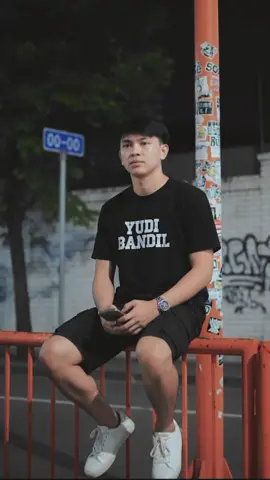 ada yang baru nih😁 prompot nya ada di bawah atau komen👇 buatkan gambar realistis 8k hd high resolution dengan ukuran foto 9:16 tanpa merubah gaya rambut dan juga wajah. seorang pria muda asia duduk di pagar oranye dengan ekspresi cuek tapi cool. ia mengemukakan kaus hitam 