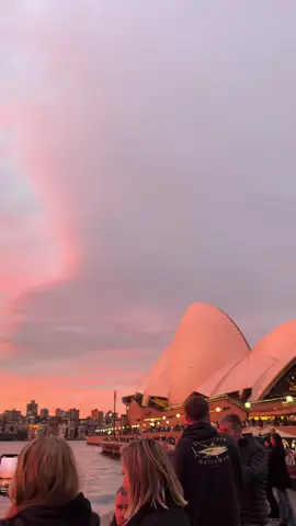 She's a stunner ✨ Tubowgule (Sydney Harbour) really puts on a show, especially during sunset when our harbour views are coated in colour ☀️  🎥: @chloe (:  📍: Warrane (@Sydney), @New South Wales  #SeeAustralia #ComeAndSayGday #FeelNSW #FeelNewSydney ID: A group of people watching a bright orange and pink sunset over Sydney Harbour as the camera pans to reveal a tall arched bridge and a building covered in white sails.