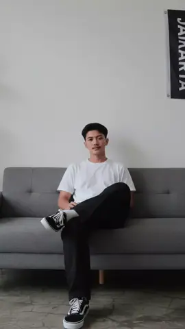 Cara edit gemini ai sedangang bergaya duduk disebuah distro jakarta.  1. buka gemini ai  2. klik (+) dikiri pojok bawah  3. dan salin promt nya  prompt : duduk santai di sofa abu-abu dengan kaki disilangkan. Ia mengenakan jaket anorak hitam bergaya streetwear dengan patch logo di lengan kiri, celana jeans hitam longgar (baggy) yang jatuh hingga menutupi sebagian sepatu, dan sneakers Adidas Samba berwarna merah marun dengan garis samping kuning. Ekspresi wajahnya santai dan cool. Latar belakang ruangan bergaya minimalis dengan dinding putih polos. Di sebelah kiri ada rak hitam berisi beberapa barang dekorasi kecil dan buku. Di sisi kanan ada bendera besar berwarna hitam dengan tulisan putih 'JAKARTA' dan logo bergaya sporty. Lantai terlihat retak-retak alami dengan tekstur semen ekspos (industrial style). Pencahayaan lembut natural daylight, menghasilkan bayangan tipis dan suasana kasual modern. Komposisi foto full-body, diambil dari sudut kamera sejajar mata (eye-level), fokus tajam, warna natural, detail realistis.