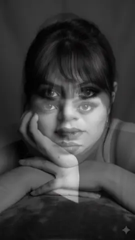 Foto IA preto e branco#########Crie para mim umA Mulher: Ela tem cabelos escuros, presos ou puxados para trás, com uma franja que cai sobre a testa. Sua maquiagem é proeminente, com destaque para os olhos, que têm um visual esfumado ou escuro. Ela está olhando diretamente para a câmera com uma expressão séria e intensa. • Pose e Composição: A mulher está com o rosto parcialmente apoiado em um braço dobrado ou em algo macio (talvez um travesseiro ou tecido). O foco principal está no rosto e na mão que está próxima à sua boca/queixo. A luz cria um forte contraste característico da fotografia em preto e branco, realçando seus traços faciais. Mantenha meu rosto original realçando a beleza natural  8k#comandosIAgemini