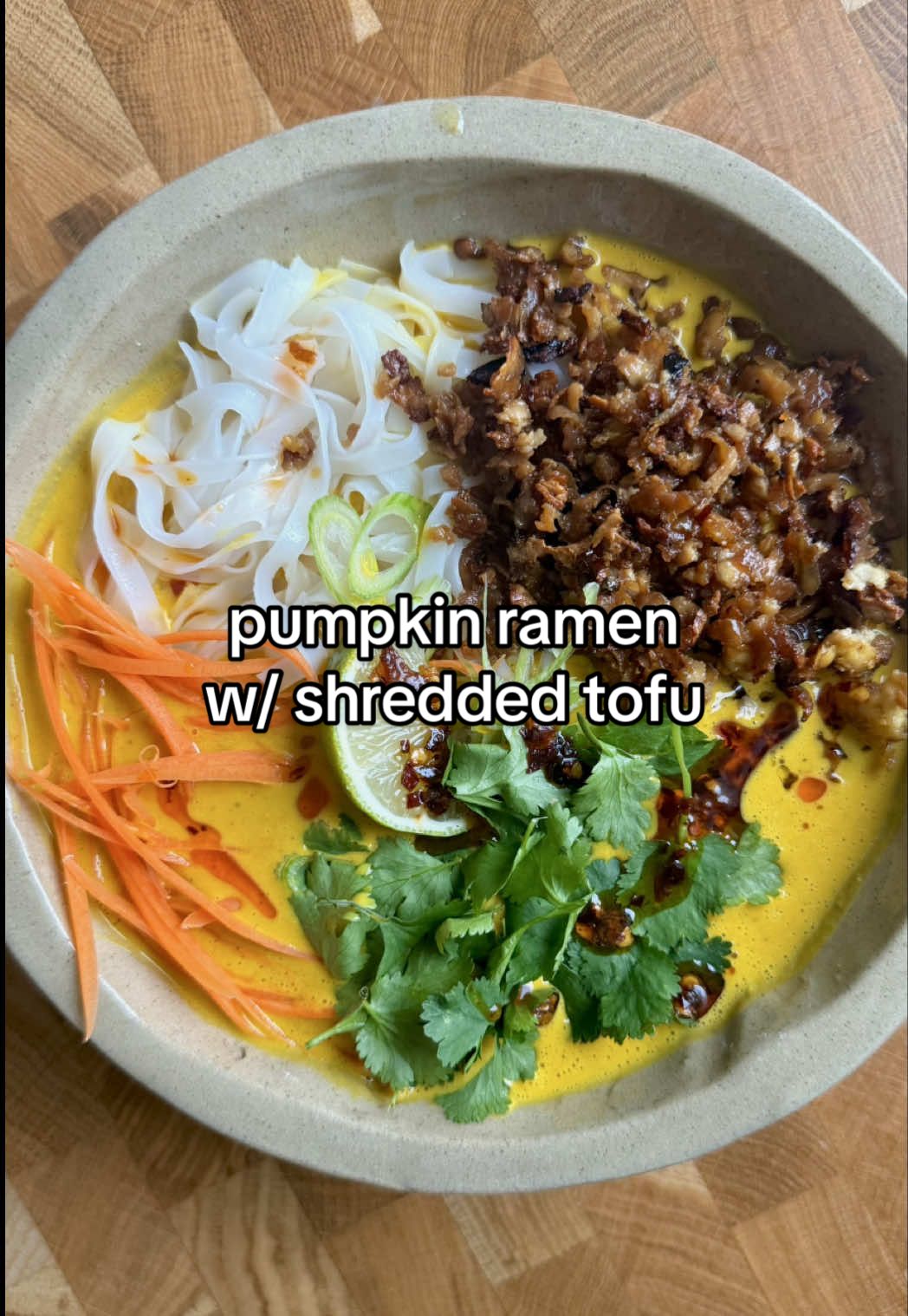 Pumpkin noodle soup on repeat allllll autumn pls 🧡 Serves 2 1/2 small pumpkin 2 inch ginger  5 garlic cloves Half tin coconut cream  350ml veg stock  1 tbsp tamari  1.5 tbsp peanut butter  1 tbsp tahini  1 lime  Rice noodles Handful Shredded carrots  Handful chopped spring onions Handful coriander  Drizzle chilli oil (I used @novicekitchen) 200g firm tofu  1 tbsp soy sauce 1 tsp maple syrup  Drizzle olive oil  Preheat the oven to 200°C fan. Peel your squash and cut it into small cubes so it roasts evenly. Toss it with a little oil, salt and pepper on a baking tray, then pop it into the oven for about 15 minutes, just until it starts to soften. To prep the tofu, pat dry and grate on the course side of a box grater. Place onto  kitchen paper and pat dry thoroughly, to ensure this gets as crispy as possible.  Once the squash is tender, take the tray out and add the ginger (just slice it into a few chunks) and the whole garlic cloves (skin on). Push everything to one side of the tray, then on the other half, add the tofu. Drizzle with the soy sauce, maple syrup and a little olive oil, tossing so everything’s coated. Bake for another 20 minutes or so, mixing to tofu 10 mins in, until the tofu turns golden and the garlic smells sweet and roasted.  When it’s all cooked and cooled slightly, squeeze the garlic out of the skin, and add to the blinder along with the squash and ginger. Add the coconut cream, peanut butter, tahini, tamari, veg stock and lime juice. Blitz until completely smooth and creamy, then taste and season well again. Pour the sauce into a saucepan and warm it through gently on the hob. Meanwhile, cook your rice noodles according to the packet instructions and drain them well. Divide the noodles between two bowls and ladle over the hot pumpkin sauce. Top with the golden tofu, shredded carrots, greens, spring onions and finish with chilli oil. 