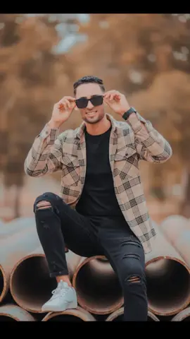 `Prompt` Hyper-ultrarealistic 8K cinematic portrait of a stylish young man standing in front of a dark industrial metal background, his face and hairstyle exactly matching the uploaded reference, hairstyle perfectly styled and set. He is facing the camera directly, with a subtle confident expression, while one hand is raised to adiust or run through his hair He wears premium black sunglasses, a black itted t shirt, a dark brown utility jacket, and dark brown cargo pants.foot wear dark brown chelsi shoes. The lightingis moody and dramatic.same as my uploaded face. `Reacts`