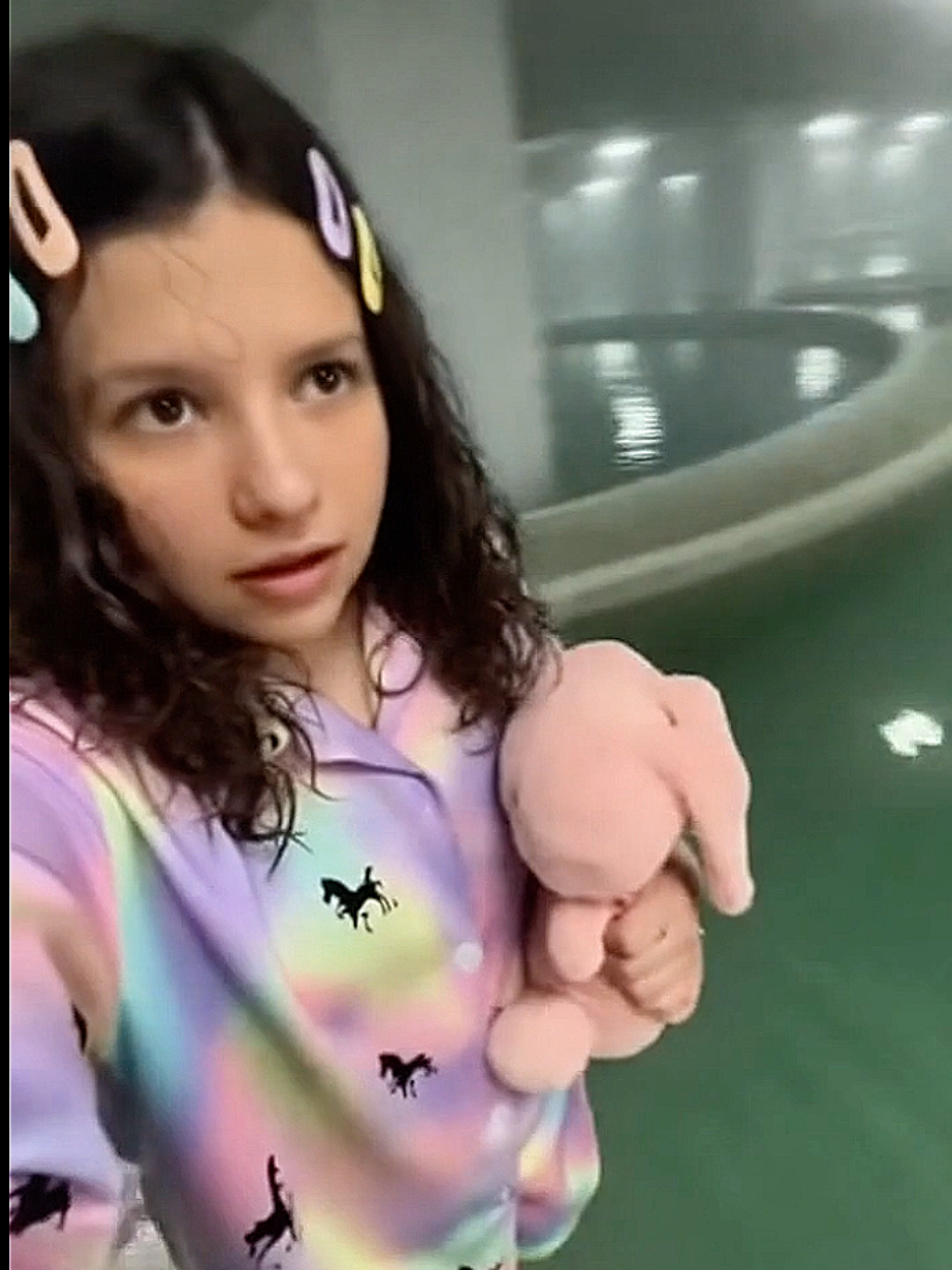 Respondendo a @xaolinmatadordepo436 Nível 37 das Poolrooms nos Backrooms: um labirinto infinito de salas interconectadas e corredores submersos em uma camada rasa de água morna e turva, que ondula com movimentos invisíveis como se algo se movesse logo abaixo da superfície, refletindo as luzes fluorescentes piscantes e falhantes no teto alto e sufocante. O chão é coberto por azulejos brancos e pretos rachados e escorregadios, com padrões geométricos repetitivos que se distorcem nas poças, interrompidos por piscinas vazias ou semi-cheias de água estagnada e negra, bordas curvas de cerâmica quebrada salpicadas de algas viscosas. No ar denso paira um vapor úmido e opressivo, impregnado com o cheiro metálico de cloro envelhecido, mofo podre e um fedor sutil de decomposição, enquanto ecos de gotas d'água pingando se misturam a sussurros indistintos e arranhões distantes, como unhas raspando azulejos. A iluminação é fraca e instável, vinda de lâmpadas fluorescentes tremeluzentes e agonizantes embutidas no forro de gesso falso, projetando sombras longas, vivas e alongadas que se contorcem nas paredes lisas e sem janelas, como se entidades sem forma as manipulassem. No centro da composição, uma figura solitária e desesperada, vestida com roupas comuns encharcadas e rasgadas, congela em pânico na água que chega aos joelhos, virando-se lentamente para encarar um corredor enevoado onde silhuetas fantasmagóricas — formas humanoides translúcidas e deformadas, com olhos vazios brilhando fracamente — emergem das sombras, estendendo membros alongados e espectrais em direção a ela, enquanto uma entidade maior e amorfa, uma massa de trevas pulsantes com tentáculos de fumaça, espreita no canto superior direito, parcialmente oculta pela névoa, evocando um terror primordial de isolamento, loucura e inevitável caçada #Backrooms #creppypasta #poolrooms #sora2 