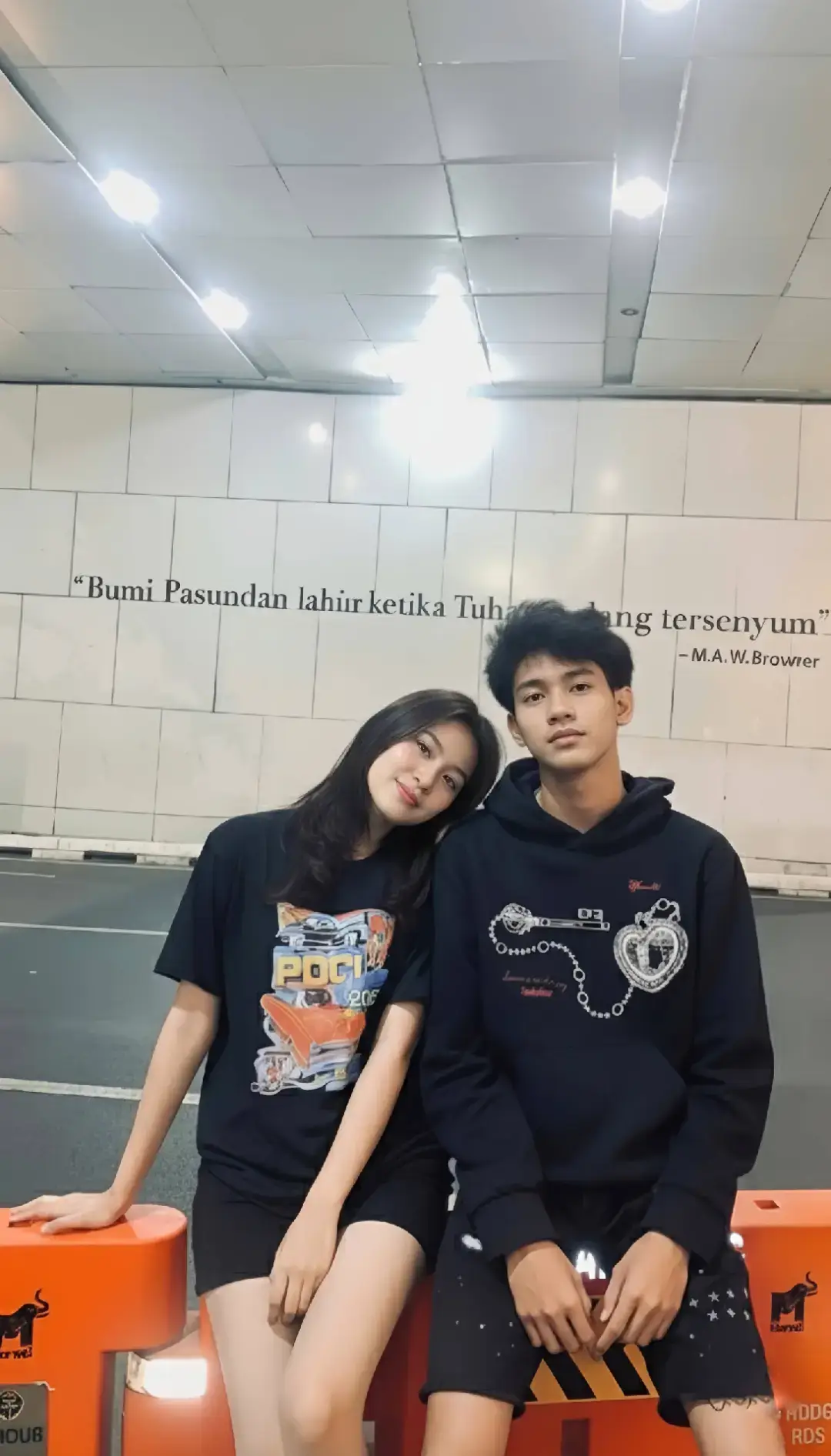 TUTORIAL BACA CAPTION‼️ Kamu pengen kaya orang-orang foto ama pasangan tapi ngga punya pacar atau mau foto bareng idola tenang sekarang ada gemini😅 Caranya? 1. Buka google/apk gemini di hp kalian 2. Masukan photo wajah kalian dan pastekan  prompt:👇🏻 Coba buatkan sebuah potret intim dan berenergi street style dari sepasang muda-mudi Indonesia dari kedua subjek di atas, duduk akrab di atas pembatas jalan oranye yang mencolok di dalam terowongan perkotaan pada malam hari. Wanita di sebelah kiri memiliki rambut panjang lurus hitam, mengenakan kaus oblong hitam dengan cetakan grafis berwarna-warni (bergaya vintage atau mobil), dan celana pendek hitam. Wajahnya menghadap ke kamera dengan senyum tipis, dan dia bersandar pada bahu pria. Pria di sebelahnya mengenakan hoodie pullover hitam dengan desain rantai dan mahkota hati berwarna perak di dada, dan celana pendek robek-robek. Pria tersebut menghadap ke kanan, menatap lembut ke arah wanita dengan ekspresi yang lebih serius atau termenung.Pasangan ini duduk di atas pembatas jalan plastik berwarna oranye terang yang mendominasi latar depan, yang bertuliskan branding lokal 