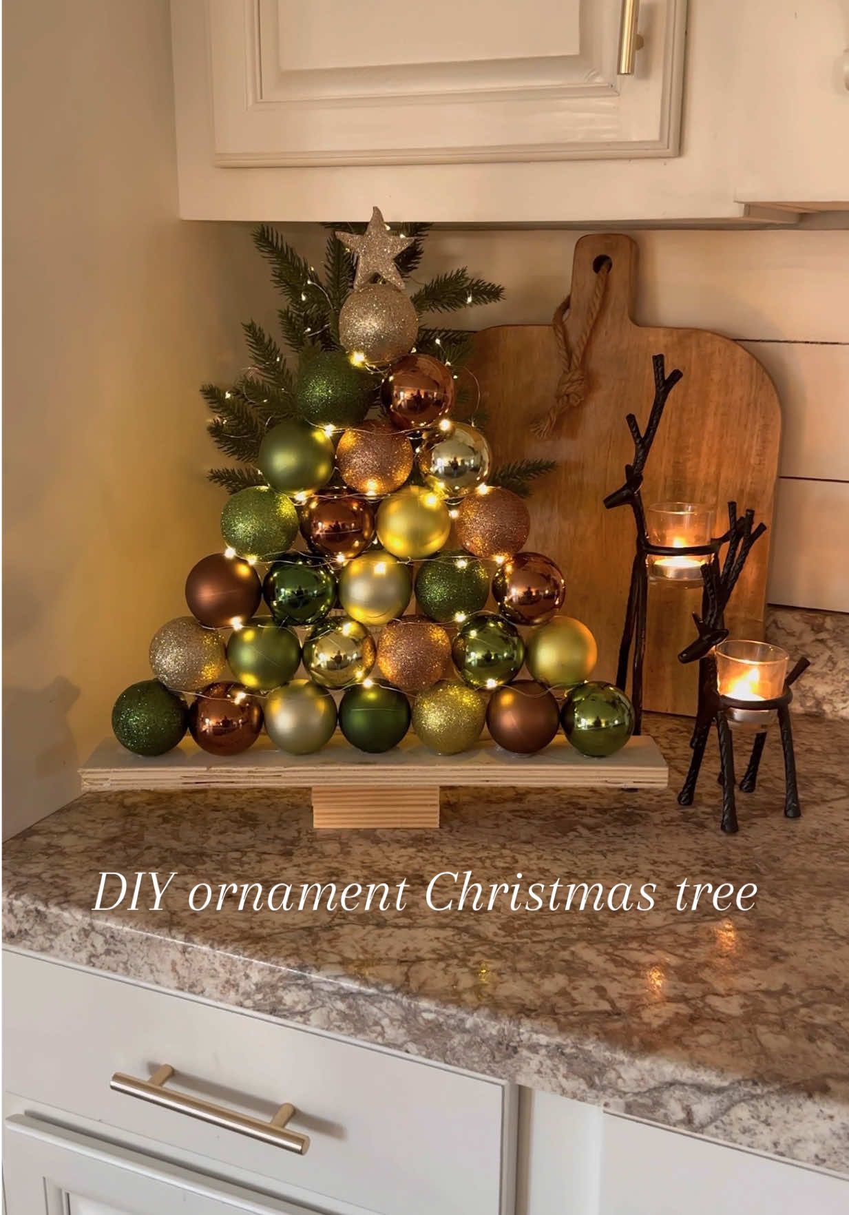 DIY ornament Christmas tree!!🎄🎄 This is so simple to make and so cute for Christmas time!!  I love how this turned out! I love the green, brown, and gold combination! It feels so warm and cozy!All you do is take the end caps off of the ornaments, glue them to a board in the shape of a tree. Wrap fairy lights around it and that’s it!! #christmas #christmasdiy #christmasdecor #diychristmas #christmastime