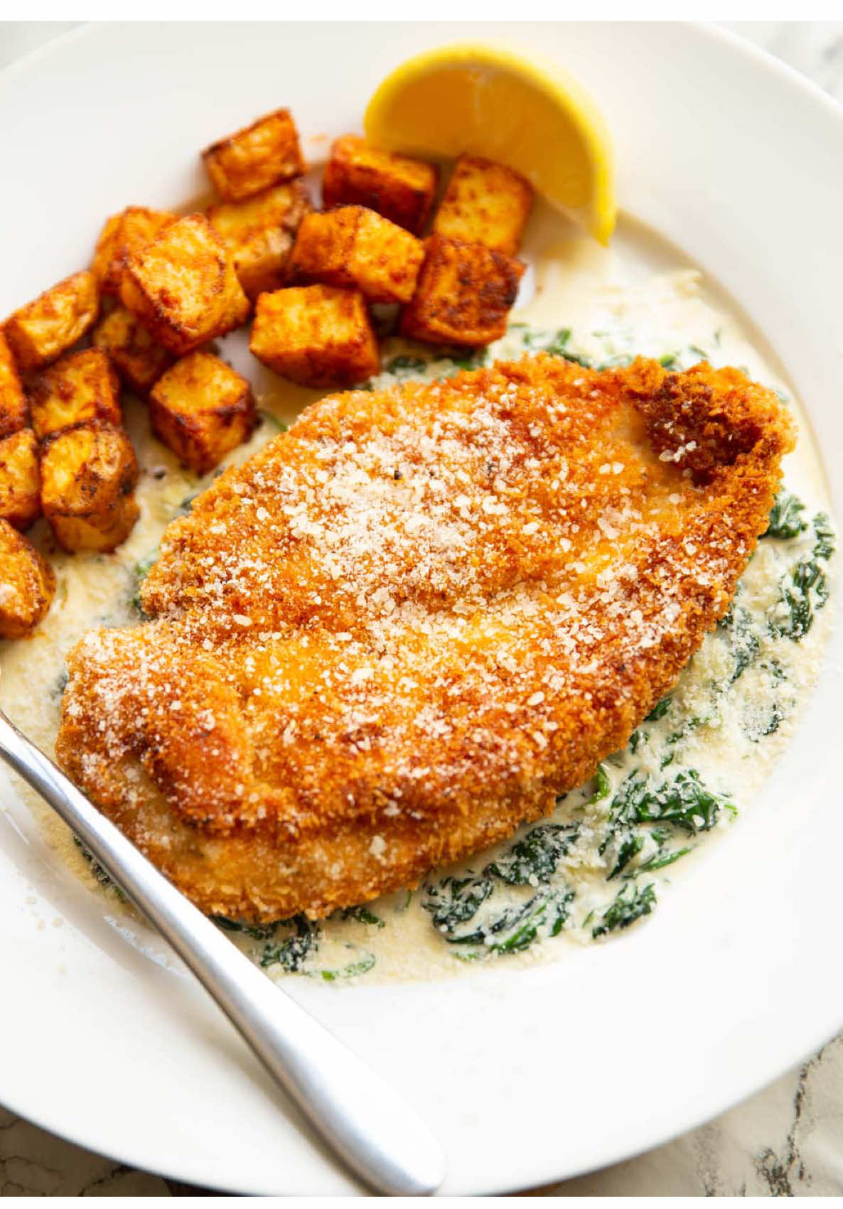 I legit haven’t stopped craving this ever since I made it. The contrast in textures, the delicious creamed spinach, the ultra crispy chicken - it’s all just so good! You’re gonna love it. If you give it a go then let me know! 😄 Chris x *Recipe in more detail on the blog CHICKEN & CREAMED SPINACH | Serves 2 INGREDIENTS ➡️CHICKEN 1x large Chicken Breast (300g/10.5oz) 1/2 tsp EACH: Salt, Italian Seasoning 1/4 tsp EACH: Black Pepper, Paprika, Onion Powder, Garlic Powder 2 tbsp Plain Flour 1 large Egg, beaten 45g / 3/4 cup Panko Breadcrumbs 120ml / 1/2 cup Veg Oil, or as needed for frying ➡️SPINACH 200g / 7oz Baby Spinach 2 tbsp Butter 1 Echalion, finely diced (sub 2x small regular shallots) 2 cloves of Garlic, finely diced 160ml / 2/3 cup Double/Heavy Cream 20g / 1/4 cup freshly grated Parmesan 1/8 tsp EACH: Ground Nutmeg, White Pepper, Salt, or to taste ➡️SERVING sprinkling of Parmesan 2 Lemon Wedges, optional METHOD ➡️SPINACH 1️⃣Add a light drizzle of oil to a large pan (or use oil spray) over medium heat then add the spinach (you may need to work in two batches). Use a wooden spoon to press down, then begin stirring until the spinach has wilted. Remove and place in a bowl to one side, then use a fork to press down on the spinach and squeeze out as much excess water as possible over the sink. 2️⃣Melt the butter into the pan then add the shallots. Fry until soft and golden, then add the garlic and fry for another 30 seconds or so. Pour in the cream then stir in the parmesan, salt, pepper and nutmeg. Simmer and stir for a couple of minutes until everything thickens, then stir in the spinach. Check for seasoning and adjust if needed. The sauce might be a little thick at the start, but the spinach should thin it back out again. ➡️CHICKEN 3️⃣Horizontally slice the chicken breast right through the centre to make 2 even-sized breasts. Lay a sheet of cling film over and use a rolling pin, mallet or heavy pan to pound the thick part to even thickness (don't go overboard or the chicken will break apart). In a small bowl combine all of the chicken seasoning. 4️⃣Line up 3 large shallow dishes: first with flour + half of the seasoning mix, second with beaten egg and third with Panko + the rest of the seasoning mix. One by one, dredge the chicken through the flour, into the egg, then in the Panko, ensuring you thoroughly coat it at each stage. Give it a gentle shake then place to one side. 5️⃣Add enough oil to comfortably coat the base of a large pan and place it over medium-high heat. Once hot (a crumb should rapidly sizzle - 180C/350F to be accurate) add both pieces of chicken and fry both sides for 3-4 minutes until golden and crispy. Timings will depend on how thick the chicken is (safe internal temp is 74C/165F for reference). Place on a wire rack with paper towels underneath to catch excess oil. ➡️SERVING 7️⃣Spoon the creamed spinach onto a large plate then place the crispy chicken on top. Add a squeeze of lemon juice if you want to, then dust over some extra parmesan. Enjoy! *I typically prep the chicken up until just before frying, then make the creamed spinach, clean out the pan and do the chicken. You can do the chicken first if you'd prefer, or even use two pans at the same time. 