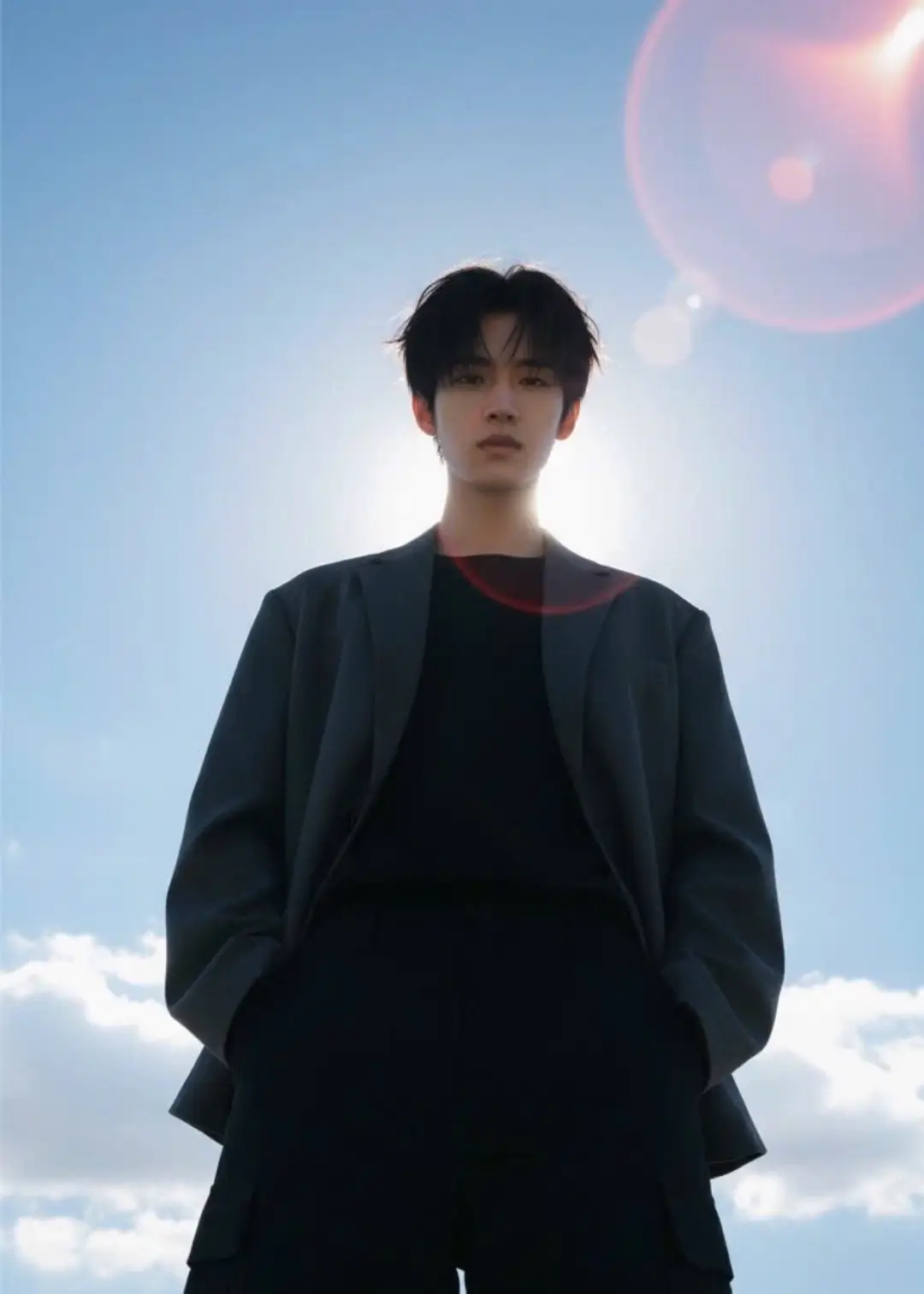 1.Open Gemini 📲  2.Upload Photo 📷  3.Paste Reminder 📃    ~• Prompt : Create a cinematic portrait (face and hairstyle remain unchanged). • Main subject: A young, dark-haired person with a confident, somewhat challenging or arrogant look. • Camera angle: Use an extreme low-angle shot, making the viewer feel like they are on the ground looking up. • Effect: This angle makes the subject appear huge, authoritative and dominant, creating a sense of dominance or respect for the character. • Posture: The subject stands upright, hands in pockets, looking down, reinforcing the arrogant or superior look. • Clothing: Wear dark clothing • Clothing color: Use neutral and dark tones, creating a strong contrast with the blue sky and bright sun, emphasizing the cool and low-key personality of the character. • Background: Completely bright blue sky with white clouds floating. The vast sky creates a sense of openness and contrasts with the heaviness of the character. • Lighting: The most important element. Strong light comes from behind and above (backlighting/rim lighting). • Sun Flare: The sun is placed in the upper right corner, shining brightly (sun flare) and causing glare. • Lens Flare: There are red/orange circles of light lined up along the beam, creating a cinematic and dramatic effect. • Shadow: Due to the light coming from behind, the front of the character is dark (silhouette-like), adding to the mystery and danger of the character. (Dark Tone)