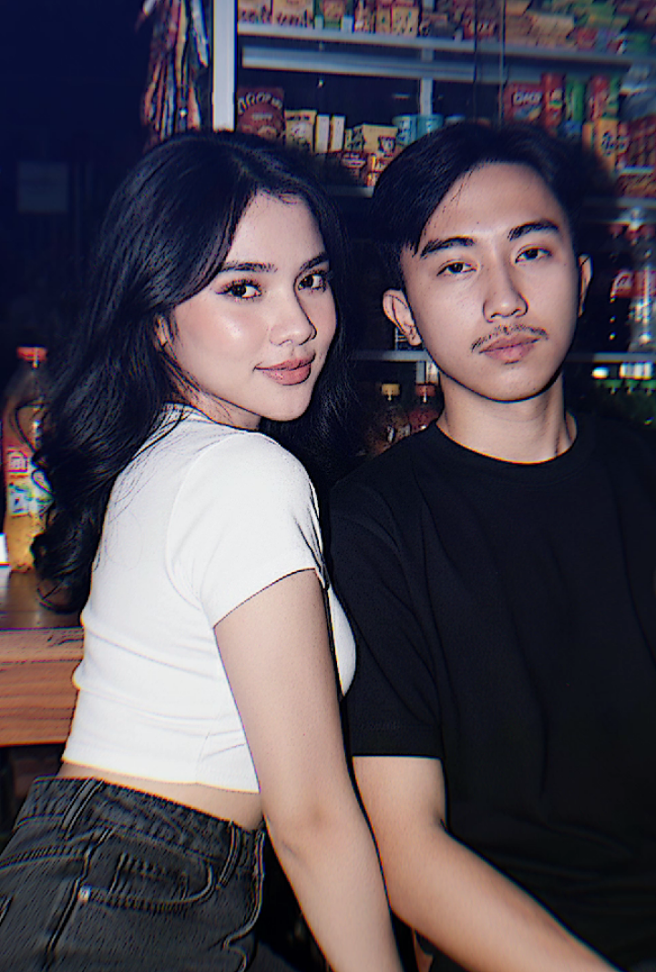 prompt Gemini ai bareng pasangan gaya vintage di warung. Buat foto wanita dan pria tanpa merubah wajah, bentuk bibir mata hidung dan gaya rambut pria dan wanita harus 100%mirip asli edit menjadi gambar  Gaya fotoristik resolusi 4k. Fokus utama foto adalah seorang pria dan wanita muda dengan rambut bergelombang . Wanita dan pria sedang duduk menyender ke kursi dan di belakang kursi terdapat meja kayu. Wanita mengenakan kaus crop top putih dengan logo bola biliar nomor 8 yang memiliki desain melingkar di bagian belakangz dipadukan dengan celana jins abu-abu gelap. Ekspresinya senyum tipis, dan pria mengenakan baju kaos hitampendek bola biliar nomor 9 dengan celana jeans abu2 gelap . Pencahayaan pada foto ini menggunakan cahaya flash langsung yang kuat, membuat wajah dan bagian depan tubuh subjek terlihat sangat terang dan menonjol, kontras dengan latar belakangnya yang lebih gelap. Efek ini menghasilkan highlight yang jelas di wajahnya, menekankan riasan dan detail pakaiannya. Latar belakangnya adalah sebuah lemari kaca atau rak di dalam sebuah toko kelontong atau warung tradisional, dipenuhi dengan berbagai produk kemasan, minuman (seperti Coca-Cola), dan produk sehari-hari. Gaya keseluruhan adalah potret modis dengan sentuhan vintage  dan efek flash yang dramatis di malam hari. Jangan merubah wajah. Foto di ambil setengah badan dari dekat wajah pria dan wanita #vintagevibes #aitrend #geminiai #fyp #foryou 