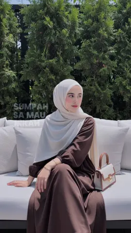 Prompt : Buatkan potret hyperrealistic seorang wanita muda jangan rubah fitur wajahnya , diluar ruangan yang estetik, seorang wanita muda dengan pasmina panjang , duduk santai di sofa putih besar dengan banyak bantal, sedikit memiringkan kepalanya. Makeup: blush on, contour pipi dan hidung, full lips Detail Pakaian dan Aksesori: Wanita tersebut mengenakan gaun modis panjang berwarna cokelat gelap. Aksesori minimalis, termasuk gelang tipis berwarna emas di kedua pergelangan tangan. Di sofa di sampingnya terdapat tas tangan kecil berwarna ivory dengan aksen kulit cokelat. Gaya, Suasana, dan Cahaya: Gaya: Minimalis, chic, santai-elegan, outdoor cafe/patio vibe. Suasana: Tenang, nyaman, berkelas, dengan nuansa hijau alami. Cahaya: Pencahayaan terik dari atas, menunjukkan bayangan, pada siang hari yang cerah. Cahaya menyorot wajah dan pakaian dengan baik. Latar Belakang dan Komposisi: Latar belakang didominasi oleh tanaman hijau terang yang rimbun dan terawat (mungkin jenis conifer atau semak tinggi) yang menciptakan dinding alami. Terdapat beberapa detail struktural gelap di latar belakang (mungkin pagar atau rangka atap). Komposisi full body yang fokus pada subject tersebut . Fotografi digital berkualitas tinggi, Fokus pada subject, dengan latar belakang bokeh / blurry di latar belakang. Ekspresi wajah yang tenang dan sedikit menoleh ke kamera.
