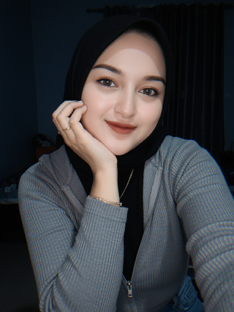 Jadikan foto Seorang perempuan berhijab hitam sedang selfie di dalam kamar pada malam hari dengan kamera ultra-wide (0,5). la mengenakan inner hitam, jaket rib tipis abu-abu, baju dalam hitam dan celana jeans biru. accesories : cincin, gelang, kalung, nailsart. Pose santai dengan mata terpejam sambil membentuk gestur hati kecil dengan tangan di pipi, ekspresi tersenyum. Interior kamar tampak gelap dengan cahaya flash kamera yang menyorot wajah. Jangan ubah wajah #geminiAI #masukberanda #fyp #trendgeminiai #ai 
