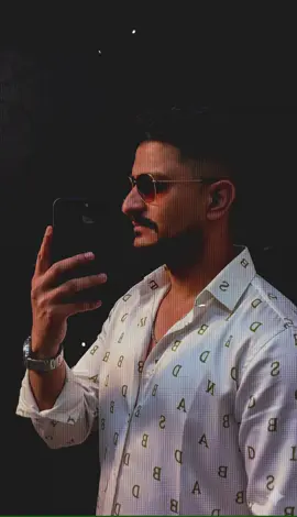 Prompt... Use 100% face above on the uploaded image. Ultra-realistic close-up mirror selfie portrait of a young man standing in a dark modern room with a black textured wall background. The camera captures him from the side profile, very close — just like a cinematic frame — his face, shoulder, and phone filling the shot. He holds a black smartphone near his cheek, fingers resting naturally on the phone edge, as he looks at his reflection with a soft, confident expression. His short black hair is style —, giving sharp volume and clean edges under the soft light. He’s wearing a white shirt with Olive Green alphabet Like ABCD printed shirt (not T-shirt), with smooth shiny fabric reflecting subtle highlights, giving a rich elegant vibe. He also wears brown sunglasses, a silver chain, a silver watch, completing his classy modern style. The lighting is soft and moody, with a warm glow sliding across his cheekbone, nose, and lips — creating deep cinematic shadows and golden reflections. Every detail — hair texture, fabric folds, skin tone, jewelry shine, and phone reflection — appears 8K ultra-detailed, cinematic, and realistic. The pose, camera angle, and framing must be identical to the reference image, only gender swapped (male), maintaining the same vibe, lighting, and composition. #djedits #gemini #growmyaccount #CapCut #views @Dibash creation @🄳🄹 🄴🄳🄸🅃🅂 
