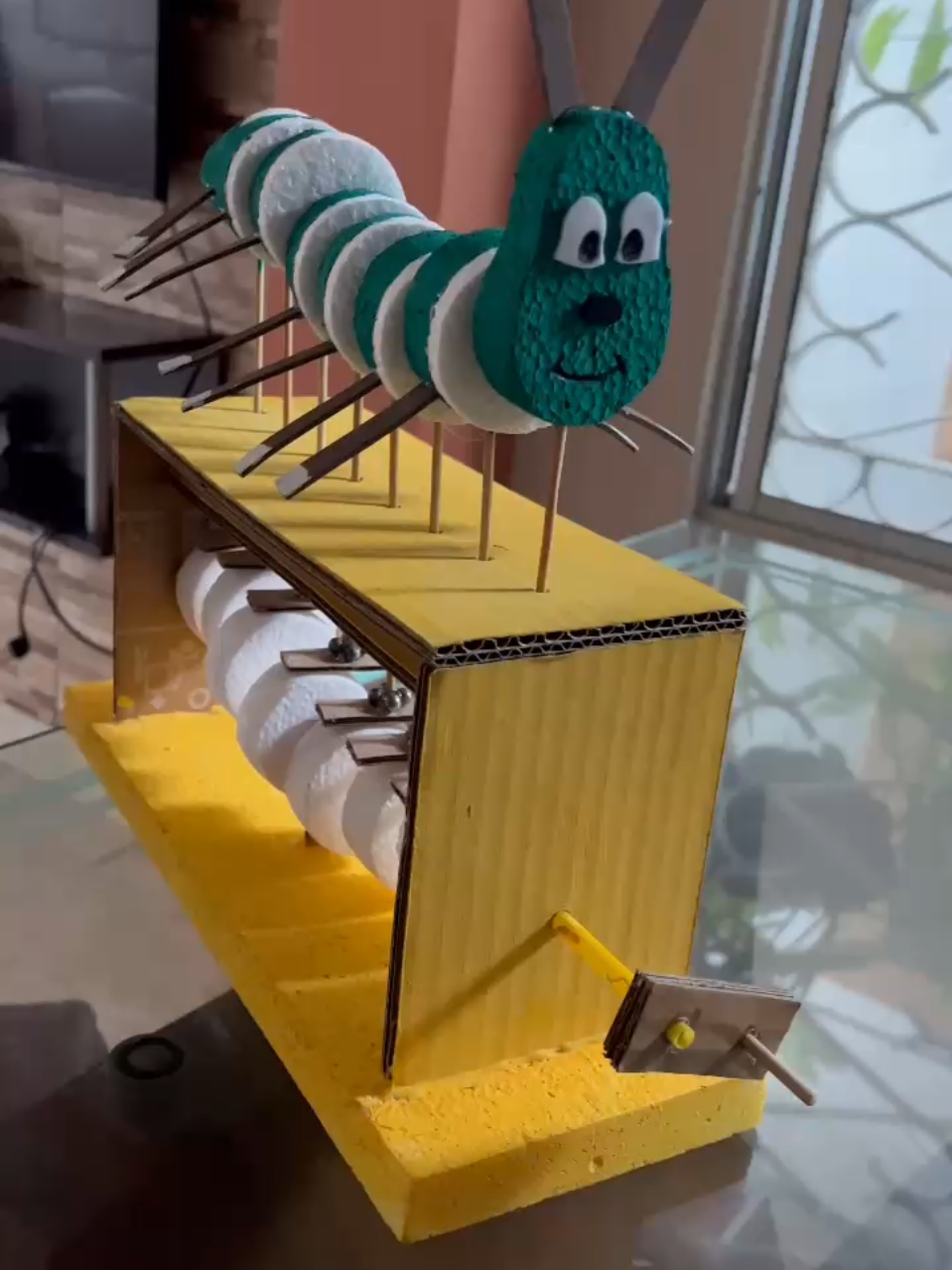 está maqueta muestra el funcionamiento básico de un sistema mecánico simple. Al girar la manivela, los ejes interiores hacen subir y bajar las varillas, generando el movimiento ondulante de la oruga. Está elaborada con materiales reciclables como cartón, palillos y esferas de icopor, combinando creatividad y principios de mecánica básica. #MaquetasEscolares #MaquetasCreativas #MaquetasMecánicas #MaquetasConMovimiento 