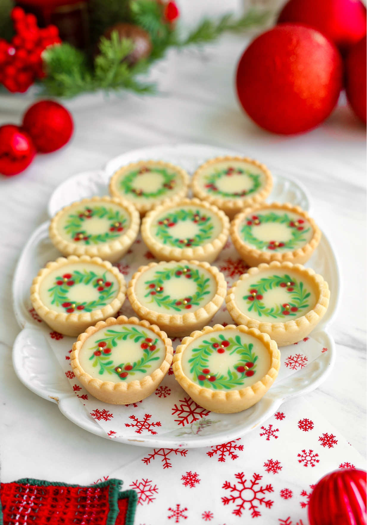 Christmas Mini Tartlets Crust •1 ⅔ cups all-purpose flour •½ cup icing sugar •A pinch of salt •½ cup unsalted butter, very cold and cubed @ paysanbreton_international  •1 egg Filling •Strawberry jam, or any jam you like •100 g white chocolate •100 g heavy cream (35% fat) @ paysanbreton_international  Method: 1.In a food processor, mix the flour, icing sugar, and salt. Add the cold butter and pulse until you get fine crumbs.  2.Add the egg and pulse again until the dough comes together. Shape it into a ball, roll it out between parchment paper to about 4 mm thick, and chill for 1 hour. 3.Grease the outer sides of cupcake molds with butter. Cut dough discs using a round cutter and place them over the molds. Freeze for about an hour, then bake at 160°C for 20–30 minutes, until golden. Let cool completely. 4.Spread a thin layer of strawberry jam inside each baked shell. 5.For the ganache, heat the cream until just boiling, then pour it over the white chocolate. Stir gently until smooth and glossy. Let it cool at room temperature for about 15 minutes, until slightly thickened. 6.Divide the ganache into small bowls. Tint a little with green and red food coloring. Pour the plain white ganache into the tart shells. Using a fine piping tip, draw small green leaves around the edges to form a wreath and add tiny red dots for berries. 7.Refrigerate for 3–4 hours until set.