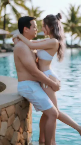 Prompt: ช่วงเวลาฤดูร้อนสุดโรแมนติกและอบอุ่นของคู่รักริมสระน้ำ ใช้ภาพที่อัปโหลดเป็นภาพประกอบใบหน้า ชายคนนั้น(ภาพตาสที่แนบไปห้ามแก้ไขหน้าตาถอดเสื้อมีพุงเล็กน้อยสวมกางเกงว่ายน้ำสีขาว ยืนพิงกำแพงหินสไตล์ชนบท อุ้มคนรักไว้แนบชิด ผู้หญิงคนนั้น(หน้าตาตามที่แนบไปห้ามแก้ไข )ผมสีน้ำตาลเทายาวรวบเป็นดังโงะ มีปอยผมด้านหน้า สวมเกาะอกบิกินี่บิดเกลียวผูกข้างสีขาวโอบแขนรอบไหล่เขา ตัวติดกัน ขณะที่ทั้งคู่สบตากันอย่างลึกซึ้ง ฉากหลังเป็นสระว่ายน้ำอันเงียบสงบ ต้นปาล์ม และแสงแดดสีทองอ่อนๆ สร้างบรรยากาศวันหยุดพักผ่อนในฝัน องค์ประกอบภาพที่สมจริงราวกับภาพยนตร์ โทนสีอบอุ่น รายละเอียดสูง แสงธรรมชาติ สไตล์การถ่ายภาพไลฟ์สไตล์#gemini #เพลงฮิตtiktok #เพิ่มเพื่อนมาเยอะๆน้า #ชุดว่ายน้ํา👙 