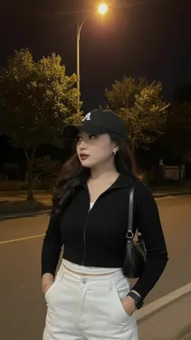 Joint Gemini Ai, prompt : Ubahlah foto tanpa merubah bentuk wajah dan riasan sedikitpun. seorang wanita cantik berkulit putih mulus pose berdiri dipinggir jalan suasa malam hari ada beberapa pohon dibelakang dan lampu jalan yg tinggi, pencahayaan dari lampu jalan, dia memakai kaos tanpa lengan berwarna putih dibalut sweater crop top  lengan panjang warna hitam pekat, dengan resleting atas sedikit terbuka, celana cargo putih high waist  jam tangan hitam, gelang kecil, kalung, anting, dan cincin, dengan rambut panjang terurai dibawahnya di curly pakai topi warna hitam dengan huruf A, sebagian rambut menutupi dada,  kualitas foto resolusi tinggi, ambil foto dari kepala sampai paha, dia menatap ke samping. Jangan ubah wajah. Pose kedua tangan di dalam saku celana , memakai tas kecil tali pendek warna hitam.  #geminiai #promptgemini 