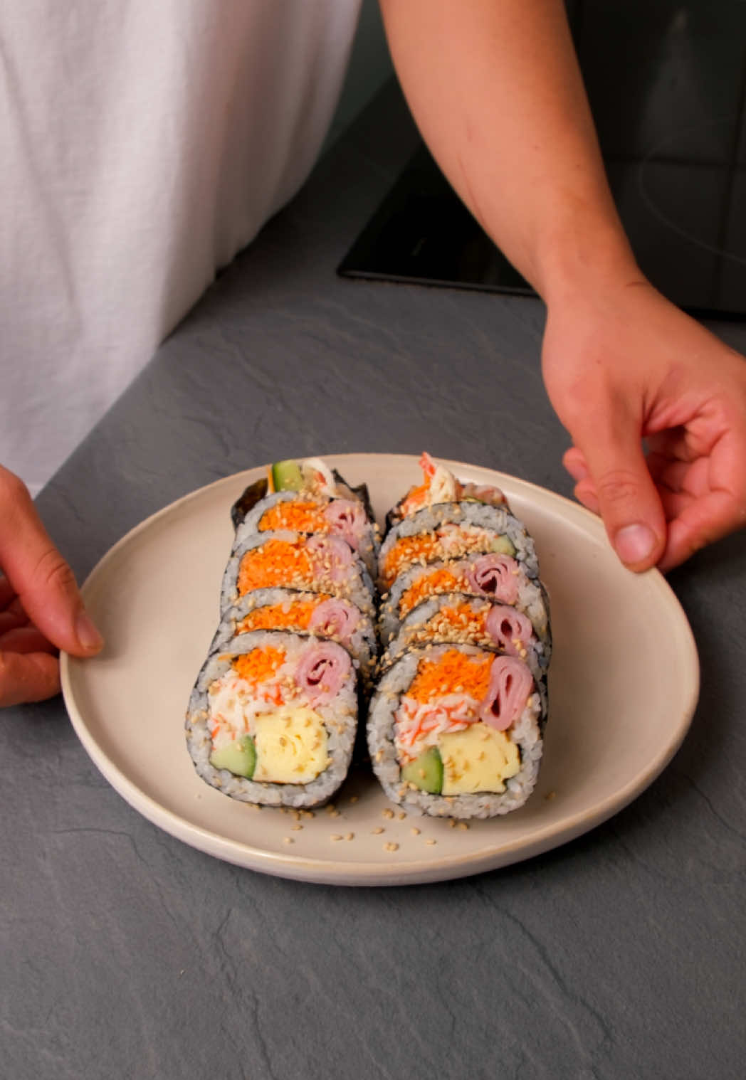 Te enseñamos cómo preparar kimbap 김밥 casero coreano como el que solía hacer mi familia en casa cuando era pequeño😊 🍽️Para 3 rollos de kimbap -Alga nori 3 hojas -Jamón cocido 150g -Arroz cocido blanco 350g -Aceite de sésamo 1 cucharada -Semilla de sésamo 1 cucharada -Una pizca de sal Para encurtido de pepino: -Pepino 200g (o 1 pepino holandes) -Azúcar 2 cucharadas -Vinagre de manzana 2 cucharadas -Una pizca de sal Para encurtido de zanahoria: -Zanahoria 150g -Azúcar 2 cucharadas -Vinagre de manzana 2 cucharadas -Sal una pizca -Surimi 100g -Mayonesa 30g -Huevos 3 uds -Agua 3 cucharadas -Sal una pizca ▫️Paso a paso: 1. Pela y corta la zanahoria y el pepino en tiras finas y alargadas. Quita las semillas del centro del pepino. 2. Mezcla las tiras con sal, azúcar y vinagre. Deja reposar al menos 30 minutos. Escurre las verduras. 3. Mezcla el arroz caliente con aceite de sésamo, sal y semillas de sésamo. 4. Corta el surimi en tiras y mézclalo con mayonesa. 5. En un bol bate los huevos con sal y un poco de agua. 6. Prepara una tortilla francesa en la sartén añadiendo el huevo poco a poco. Para que quede compacta. Deja enfriar la tortilla y córtala en tiras. 7. Sobre una tabla, coloca una hoja de alga nori con el lado brillante hacia abajo. Extiende el arroz por encima, presionando un poco más de arroz en la parte superior para sellar bien al enrollar. Coloca media hoja de alga nori adicional encima. 8. Añade todos los ingredientes (surimi, pepino, zanahoria, huevo y jamón cocido) y enrolla con cuidado, presionando con firmeza para que quede compacto. 9. Dale unas pinceladas de aceite de sésamo al kimbap y córtalo en rodajas del grosor de un dedo.  10. Emplata el kimbap y espolvorea un poco de semillas de sésamo por encima. ✅Tip - Los encurtidos de zanahoria y pepino se pueden preparar el día anterior; duran más de una semana en la nevera. - Una vez cocinado el arroz y la tortilla, deja que se enfríen al aire antes de colocarlos sobre el alga. -¡Después de cortar el kimbap enróllalo en papel de horno y pon papel de aluminio en el exterior si quieres transportarlo! #kimbap #gimbap #koreanfood #comidacoreana #corea 