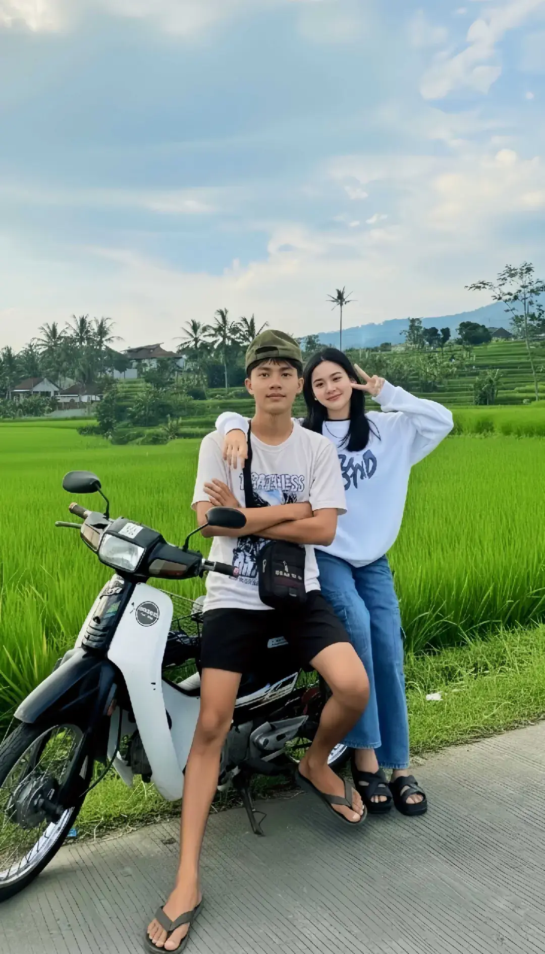 TUTORIAL?? BACA CAPTION‼️ Caranya? 1. Buka google/apk gemini di hp kalian 2. Masukan photo wajah kalian dan pastekan  prompt:👇🏻 Coba buatkalah sebuah foto vertikal dengan kualitas gambar yang tajam dan berdefinisi tinggi, diambil dengan pencahayaan alami yang cerah di luar ruangan, kemungkinan besar selama 'jam emas' (sore hari) karena warna yang jenuh dan hangat. Komposisi terbagi rapi, dengan subjek manusia dan kendaraan mendominasi sepertiga bagian bawah, dan pemandangan alam mengisi dua pertiga bagian atas. Subjek dan Aksi: Dua remaja - seorang pria dan seorang wanita - berpose santai di tepi jalan aspal yang berbatasan langsung dengan sawah. Pria tersebut, mengenakan kaus putih bergambar/bertulisan dan celana pendek hitam, duduk di atas sepeda motor bebek klasik berwarna putih-hitam, menyilangkan kedua tangan di dada dengan ekspresi tenang. Ia melengkapi penampilannya dengan topi camo terbalik dan sandal jepit. Di sebelahnya, wanita tersebut berdiri, bersandar dengan akrab ke bahu pria. Ia mengenakan sweater putih berlogo atau tulisan, celana jeans biru, dan sandal. Tangan kirinya melingkari bahu pria, sementara tangan kanannya berpose 'jari V' (simbol damai) di dekat wajahnya, memberikan sentuhan playful pada foto tersebut. Latar Belakang dan Kedalaman: Latar tengah didominasi oleh hamparan sawah padi hijau yang sangat luas dan subur, memberikan tekstur visual yang kaya dan warna hijau vibrant yang kontras dengan pakaian putih subjek. Latar belakang menunjukkan lapisan kedalaman, dimulai dari deretan pohon kelapa tinggi dan rumah-rumah penduduk di kejauhan, hingga siluet perbukitan yang menjulang di bawah langit. Langitnya berwarna biru muda yang cerah, dengan beberapa awan putih tipis yang tersebar, menandakan hari yang cerah dan cuaca yang baik. Nuansa dan Estetika: Foto ini memiliki nuansa tropis, damai, dan youthful (berjiwa muda), mengombinasikan gaya hidup kasual anak muda dengan keindahan alam pedesaan Indonesia. Estetika keseluruhan cenderung cerah, bersih, dan berorientasi lifestyle, ideal untuk media sosial, menekankan hubungan subjek dan harmoni dengan lingkungan alam sekitarnya. 3. Tunggu hasilnya 4. Kalo sudah sesuai Download nahh sekarang kamu udh ngga bakal dihina lagi Bree👍🏻🤍 @zee asadel  #prompt #geminiai #fyp #honda #astrea 