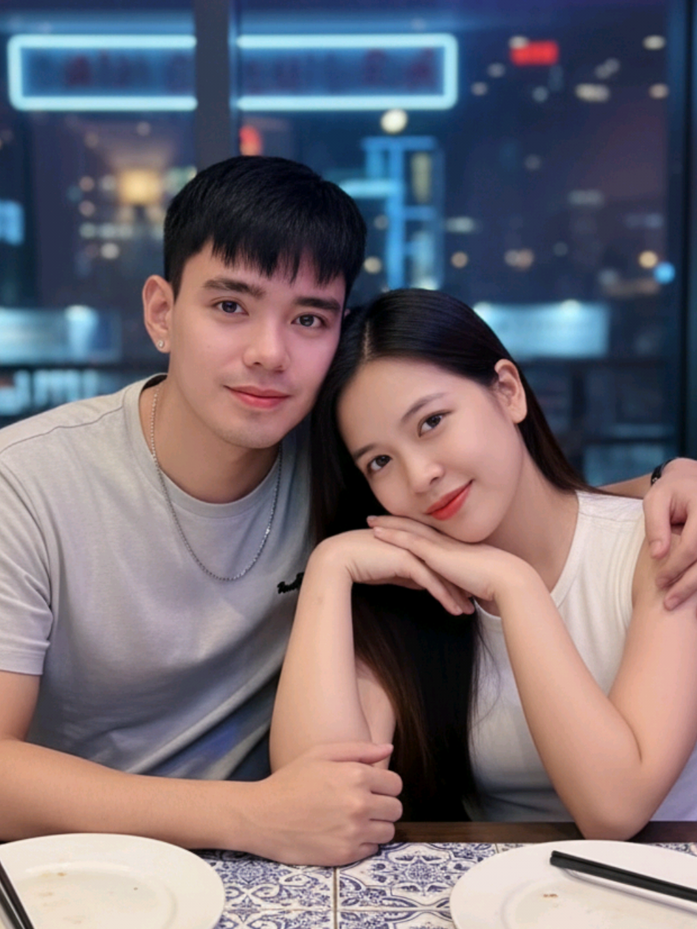 ❤️❤️❤️  @ᑕнᴏɴ’ᑕнᴏɴッ  Prompt: Edit photo from this image A young couple sitting close together at a night café with a romantic atmosphere. The man has his arm around the woman, both smiling softly at the camera. The woman has long straight hair, natural makeup, and rests her face gently on her hands. She wears a white sleeveless top, while the man wears a light gray t-shirt with a small logo and a simple necklace. The background features blue and purple neon lighting, city lights, and a slightly blurred night skyline. The table in front of them has patterned tiles, adding a cozy and aesthetic vibe. The mood is warm, intimate, and modern with a dreamy, cinematic feel. #fyp #foryoupageofficial #couplegoals #couple #coupleai 