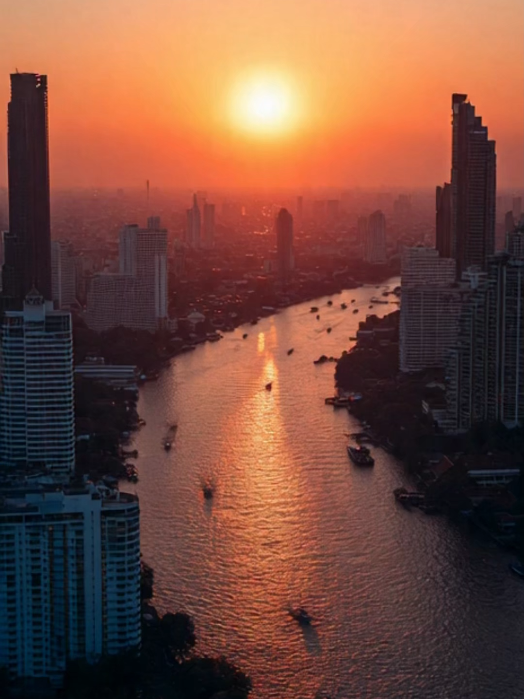 Experience the golden calm of Bangkok at sunset 🌇🇹🇭 — a smooth aerial flyover reveals the Chao Phraya River winding through the city, where golden temples like Wat Arun and Wat Phra Kaew glow along the riverbanks. Skyscrapers fade into a soft orange haze as boats glide below and reflections shimmer on glass towers and water. The humid tropical air glows with warm light — a peaceful transition from day to night, capturing the tranquil yet vibrant soul of Bangkok. 🌅✨ #Bangkok #ChaoPhrayaRiver #GoldenHour #ThailandVibes #CinematicAmbience