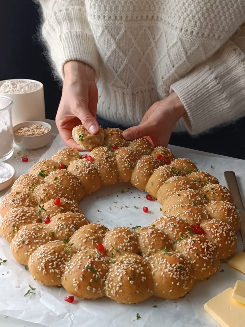 Add a festive touch to your holiday table with this GF Sourdough Dinner Roll Wreath ❤️ Soft, fluffy, and filled with your favourite cheese, these rolls are baked to golden perfection and brushed with parsley butter. Serve them warm, garnished with fresh herbs or cranberries, for a show-stopping centerpiece everyone will love 🎄✨ Levain: 60 g sourdough starter, 100% hydration 120 g water, at room temperature 60 g brown rice flour 60 g light buckwheat flour Dough: 370 g water, at room temperature 22 g psyllium husk 300 g ripe levain 35 g extra-virgin olive oil or butter or vegan butter, melted and cooled 25 g honey (optional) 110 g corn flour (US) / maize flour (UK) 80 g GF oat flour 60 g potato starch 40 g cornstarch (US) / cornflour (UK) 11 g sea salt Assembling the bread rolls: 110–180 g (vegan) cheese, cut into 3-5 g cubes 2 tbsp soy milk mixed with 1 tbsp maple syrup sesame seeds Parsley butter: 2 tbsp extra-virgin olive oil or melted butter or vegan butter  1 tbsp parsley, finely chopped  To decorate: pomegranate seeds or cranberries fresh thyme or rosemary Build the levain: Weigh 60 grams of active starter in a clean jar, then add the water and whisk together. Add the flours and mix until smooth. Ferment the levain for 6-8 hours, or until it is bubbling and it has risen to a peak, before mixing it into the dough. Make the dough: 1. In a bowl, whisk together the water and psyllium husk powder. Whisk vigorously until it’s fully incorporated and starts to thicken. Set aside for about 10 minutes to form a gel. 2. Add the ripe levain, honey and olive oil or melted butter to the psyllium mixture and mix until everything is well incorporated.  3. In a large bowl, mix together the flours, starches, and sea salt. Add the psyllium mixture to the dry ingredients and knead either by hand (I recommend using a large wooden spoon) or with a stand mixer for 5-8 minutes, until the ingredients are fully incorporated and the dough is smooth.  4. Transfer the dough to a work surface and divide it into 36 pieces of about 28-29 g each. Work with one piece at a time, keeping the rest covered with plastic wrap. Flatten each piece slightly, place a cheese cube in the center, fold the dough around it, pinch to seal, and roll into a tight ball. If the dough is sticky, lightly coat your hands and work surface with olive oil.  5. Place the rolls seam-side down on a baking sheet lined with parchment paper. Arrange 20 rolls in a circle with an inner diameter of 22 cm. Place the remaining 16 rolls inside the circle. Cover to prevent the dough from drying out and proof at room temperature for 3-5 hours. The bread rolls won’t double in size but should expand and puff up. 6. About 45 minutes before baking, preheat the oven to 240°C. Once the bread rolls are finished proofing, brush them with the milk and maple syrup mixture and sprinkle with sesame seeds. Place the bread rolls on the middle oven rack and reduce the temperature to 210°C. Bake for 25 minutes until golden brown on top.  7. In a small bowl, mix the olive oil or melted butter with the finely chopped parsley. Brush the bread rolls with the mixture while they’re still warm.  8. Allow the wreath to cool for about 10 minutes before decorating with cranberries or pomegranate seeds and fresh thyme or rosemary. The bread rolls are best served while they’re hot or warm. Enjoy!  #glutenfree #glutenfreesourdough #sourdough #breadart 
