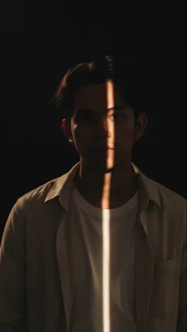 Gemini AI PROMPT: 1. Open Gemini App/Website 2. Upload Your Photo 3. Copy & Paste this prompt: standing in a dark studio with a single narrow beam of warm light cutting vertically across his face and chest, creating a striking contrast between light and shadow. The man has slightly tousled dark hair and light stubble, wearing a beige or off-white overshirt with a white inner T-shirt. The light strip falls perfectly along the center of his face and continues down to his torso, illuminating fabric textures and facial contours. The background is completely black, emphasizing the dramatic lighting. The mood is mysterious and moody, with realistic skin tones, soft highlights, and fine detail in shadows. Hyper-realistic, 8K, DSLR photography style, cinematic lighting, moody atmosphere. 100% use my upload reference image image generate   #gemini #prompt #aesthetic #photography #ai