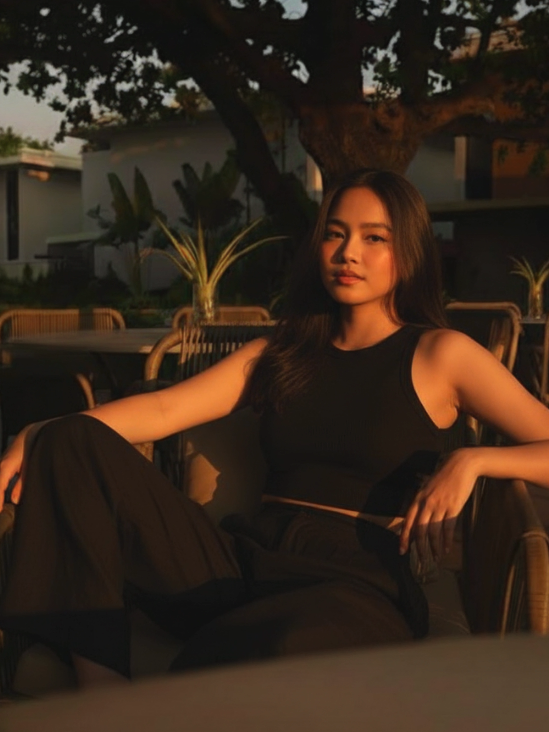 1. Open Gemini App/Website 2. Upload Your Photo and photo of the location. (see comments for photo link of exact location) 3. Copy & Paste this prompt: Three-quarter length, moody golden-hour environmental portrait of me (preserve my facial features i should be recognizable) lounging comfortably in an outdoor resort setting, photographed on iPhone 15 Pro with the main wide camera in warm natural sunset light, no background blur. She is seated on a modern woven armchair, one knee raised to her chest and one arm resting casually on the chair’s armrest. She wears a black cropped tank top, and matching wide-leg pants. Warm sunlight illuminates one side of her face and body, casting rich, elongated shadows while the background features shady trees, leafy plants, and modern outdoor furniture in soft focus. The image showcases deep orange highlights, natural skin tones, clean texture detail, and high dynamic range typical of iPhone computational photography, accurately rendering both highlighted and shaded areas without any artificial depth effect or background blur. Do not over-edit or enhance the face or expression in any way. Maintain a high degree of facial fidelity to the provided image. avoid background blur. ive provided the exact bg