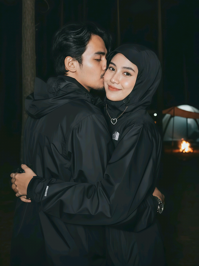 Sepasang kekasih (dengan referensi wajah, telinga, hidung, mulut dari gambar pertama, 100% realitas virtual) berada dalam pelukan lembut di tengah malam yang sunyi. Ambil bidikan close-up dari belakang, hanya memperlihatkan wajah mereka yang saling mendekat, diambil dengan lensa RF 85mm pada kamera full frame, aperture f/1.4, resolusi hingga 8K. Pencahayaan flash yang kuat ala kamera digital awal 2000-an menciptakan kontras yang realistis dan profesional, dengan cahaya kabur yang menonjolkan ekspresi wajah yang tenang dan damai. Banyak butiran halus menambah sentuhan nostalgia pada foto snapshot awal 2000-an ini. Cahaya flash memancar lembut pada wajah mereka, membuat kulit memantulkan kilauan yang bersih, cerah, putih, dan halus. Wanita muda itu mengenakan jaket gorpcore hitam yang tudungnya menutupi rambutnya, dengan logo North Face putih dan kalung berbentuk hati yang terlihat di dadanya. Pria di sampingnya juga mengenakan jaket gorpcore hitam dengan logo North Face putih, jam tangan Rolex, dan kalung berbentuk hati yang serasi. Di latar belakang, hutan pinus yang gelap menjadi saksi bisu keintiman mereka. Jauh di kejauhan ke kanan, tenda dan struktur kanvas putih yang didirikan di area berkemah terlihat samar, diterangi oleh cahaya api unggun yang menyala, menambah suasana hangat dan romantis. Wanita itu mengambil selfie dengan kamera belakang di tangannya, wajahnya sedikit menoleh ke kamera dengan senyum lembut yang playful, imut, dan ramah, seolah berbagi rahasia kecil dengan dunia. Mereka sangat berdekatan, hampir tak ada jarak di antara keduanya. Cahaya flash menerangi wajah mereka dari depan, sementara latar belakang tetap gelap, menciptakan aura misterius dan penuh cinta. Pastikan wajah mereka tetap semirip mungkin dengan referensi awal. #capcut #geminiai #fypシ゚ 