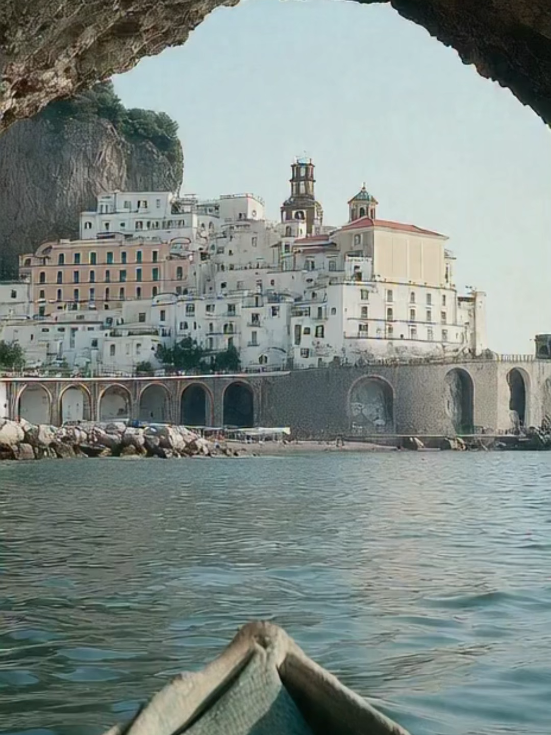 Atrani Boat Arrival – Sunset Serenity Low-angle view from a small Italian boat gliding into Atrani as pastel buildings glow under the fading sun. Stone arches frame the entrance while gentle waves reflect warm Mediterranean light, creating a calm coastal moment. #AtraniItaly #amalficoastitaly #MediterraneanTravel #SunsetHarbor #ItalyCoastline