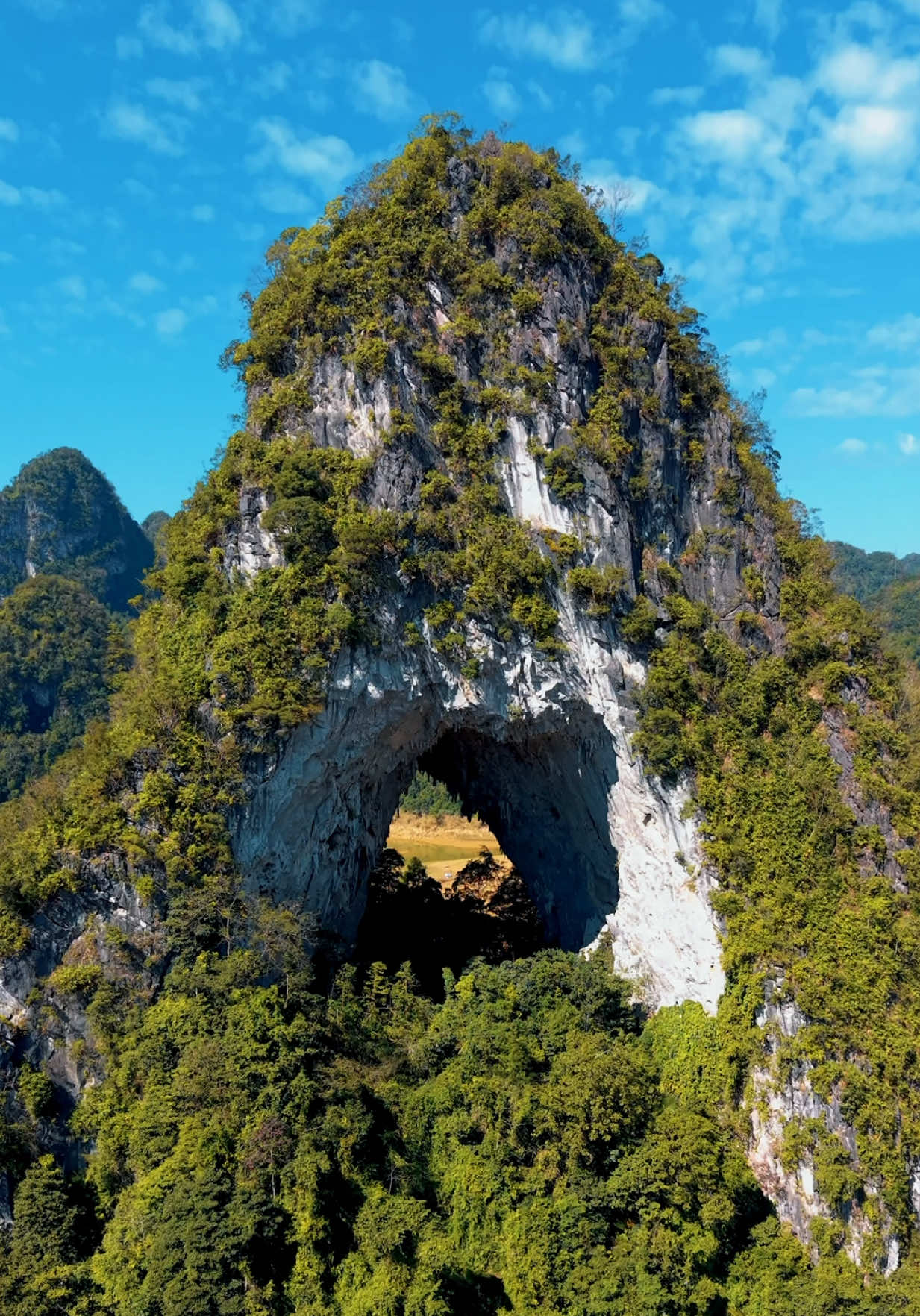 Núi Mắt Thần blends into this magical valley in Cao Bằng, where a giant round hole cuts straight through the mountain like an actual eye 👁️✨ 	•	Locals call it Núi Thủng – “the pierced mountain” 	•	It’s over 400 million years old 	•	Part of the UNESCO-listed Non Nước Cao Bằng Geopark 🌍 #caobang #godseye #heavensgate #dulichvietnam #flycamvietnam 