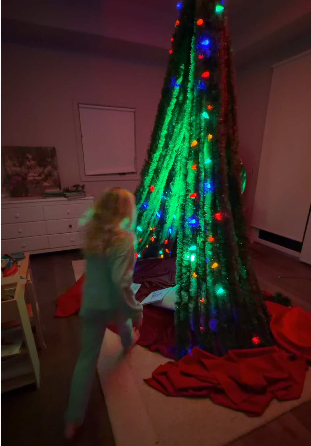 Here’s how this is the easiest Christmas tree I’ve ever put up. (Read caption for how.) My daughter asked to sleep under the Christmas tree… so I built one she could actually live inside. What I didn’t expect was that it would turn into the most-used thing in the house all week. Sounds ridiculous, but I used 500 feet of lightweight green garland (10 packs of 50 ft). The funny thing is: when you pile that much of it together, it suddenly looks like you knew what you were doing. (You don’t. I didn’t. That’s the magic.) I hung all of it from a pulley in the ceiling where the fan used to be which sounds dangerous, but every dad has a ceiling fan they regret removing, so I figured why not get some use out of that hole. As soon as I pulled it tight we were almost done. Wrapped some Christmas lights around the same center point. Instant glow. Looked like a scene from The Grinch. Then came the Gorilla Tape around the base to lock the garland to the floor. And yes this is the part where I realized how stupidly easy this whole thing was. It’s basically a kids fort with tinsel instead of couch cushions. Inside, I threw down an old tree skirt. Outside, I used a few red tablecloths as trim, mostly because they were the first red things I grabbed and I refused to overthink it. When the lights went off, it looked steller. It became our nightly story spot. And then my favorite part I kept finding my 9-year-old in there alone, playing house inside a Christmas tree like it was the most normal thing in the world. That’s when you know you built something worth keeping around. Totally worth it. You should build one.