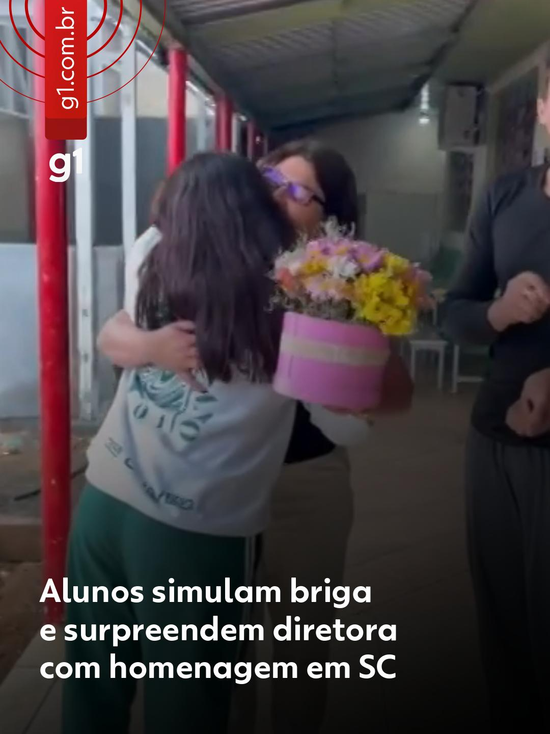 Surpresa de aniversário - A diretora Glenda Rosa Zanchett, de 48 anos, foi surpreendida por alunos do 9º ano de uma escola pública em Fraiburgo, no Oeste de Santa Catarina. Eles encenaram uma briga para chamar a atenção dela e, em seguida, surpreendê-la com uma homenagem pelo Dia do Diretor. O vídeo da encenação viralizou nas redes sociais e já ultrapassou 1,7 milhão de visualizações até terça-feira (2). Nas imagens, dois estudantes simulam uma discussão e começam a se empurrar. Quando Glenda chega para apartar o conflito, uma aluna aparece com um buquê de flores e a diretora se emociona. Depois, os alunos se juntam em um abraço. Ao #g1, Glenda contou que a homenagem foi feita em 13 de novembro, após a turma retornar de uma viagem. Segundo ela, a surpresa foi completa e nunca havia registrado uma briga na escola, então acreditou que se tratava de uma agressão real. A diretora explicou que trabalha na unidade há seis anos e mantém uma relação próxima e equilibrada com os alunos, baseada em diálogo, cobrança e afeto. “Eu confesso para você que foi uma mega surpresa. Quando eu me deparo com aquela cena, eu realmente achei que era briga”, afirmou. Veja os detalhes em 'leia o artigo'. #g1local #santacatarina #diretora #escola #santacatarina
