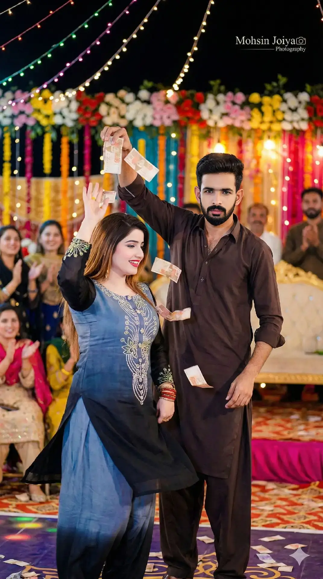 A vibrant and realistic photograph depicting a cultural stage performance in Pakistan . A young man from refrence photo, mid-20s, with a joyful expression, is actively showering Pakistani rupee notes (currency) over a beautiful female dancer( from refrence photo) on stage. The dancer, in her late 20s, is wearing same dress like Refrence Photo , performing an energetic dance move. Her expression is graceful and appreciative. The setting is a brightly lit outdoor stage at night, possibly a wedding reception or a local village festival, with colorful string lights, floral decorations, and a cheerful audience in the blurred background. Focus on the dynamic movement of the money in the air and the interaction between the man and the dancer. Sharp focus on subjects, bokeh background, warm lighting.